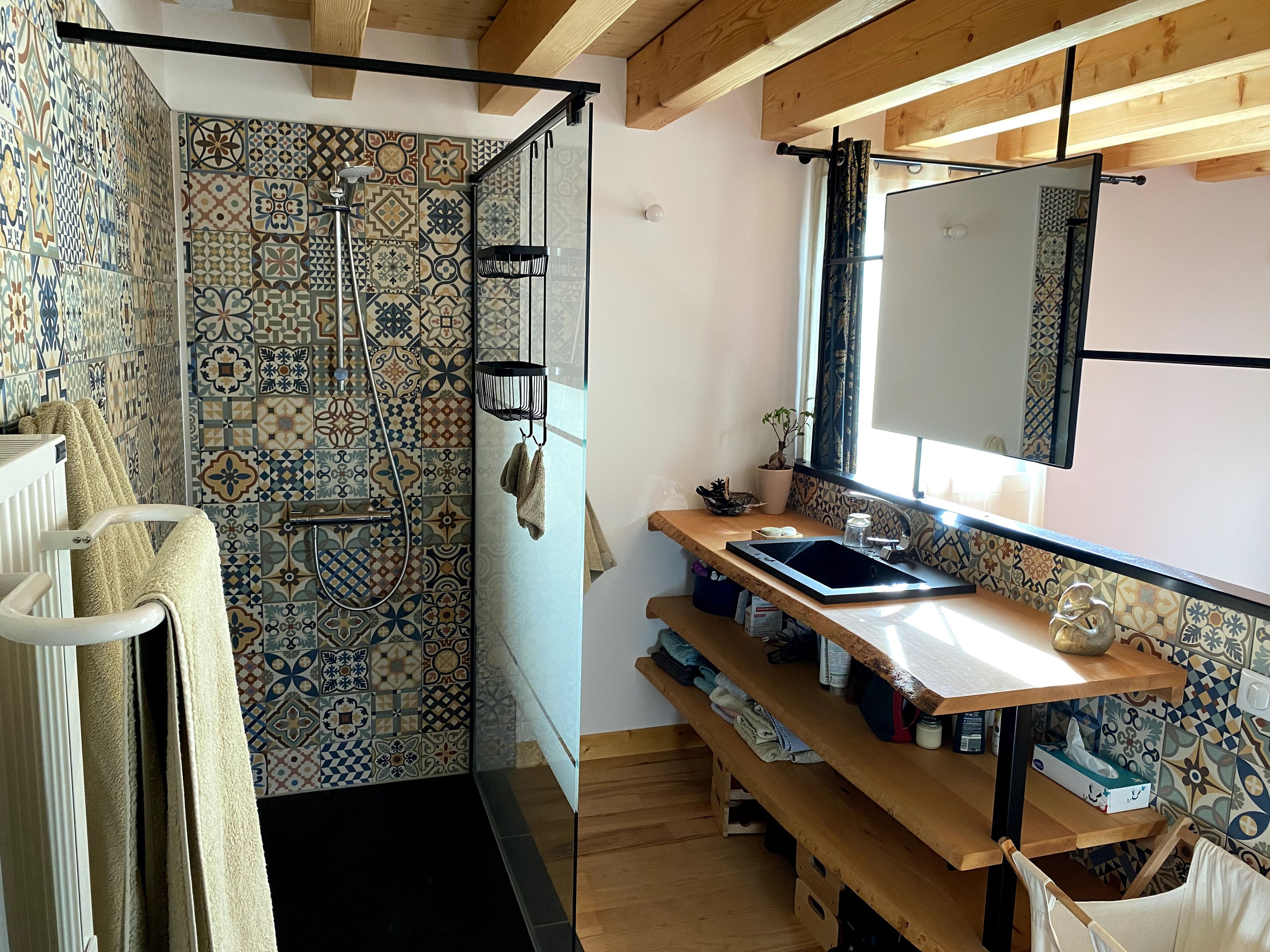 A bathroom with a shower, a towel rack, a sink, and a window with a view.