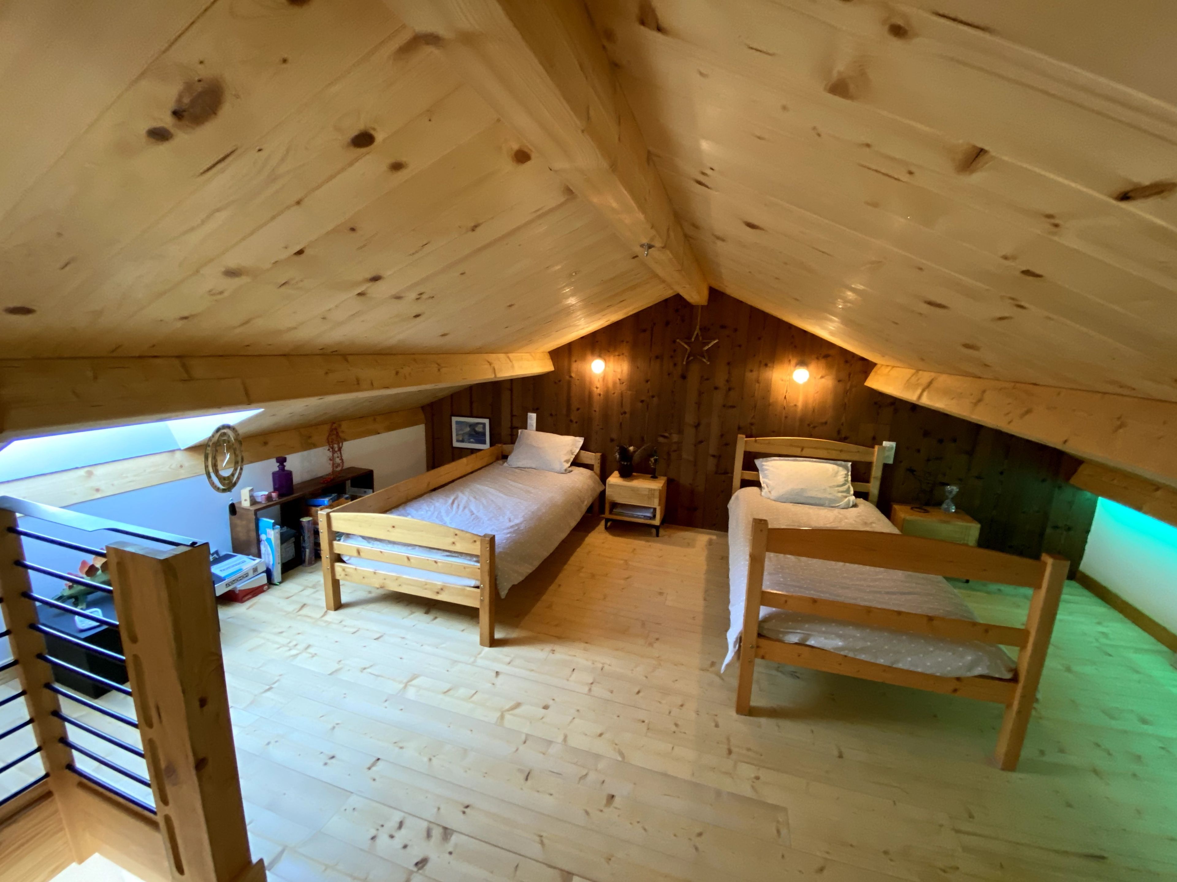 Un dormitorio de ático con piso de madera, dos camas, una mesita y una estantería.
