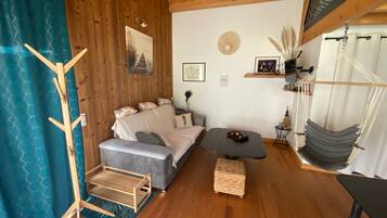 A cozy room with a sofa, a small table, a hanging chair, and a wooden floor.