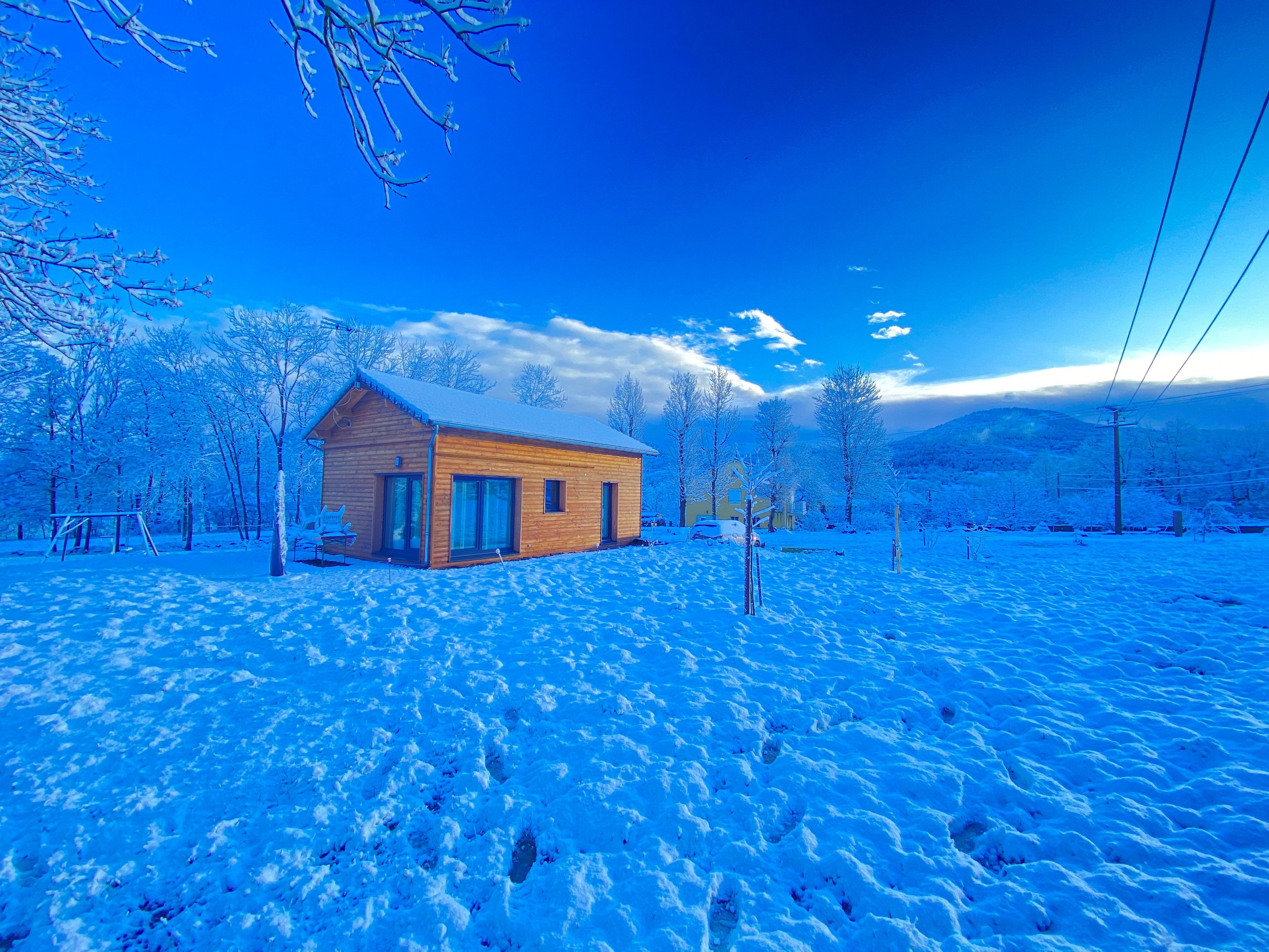 Una cabaña de madera con techo nevado, rodeada por un paisaje invernal y árboles.