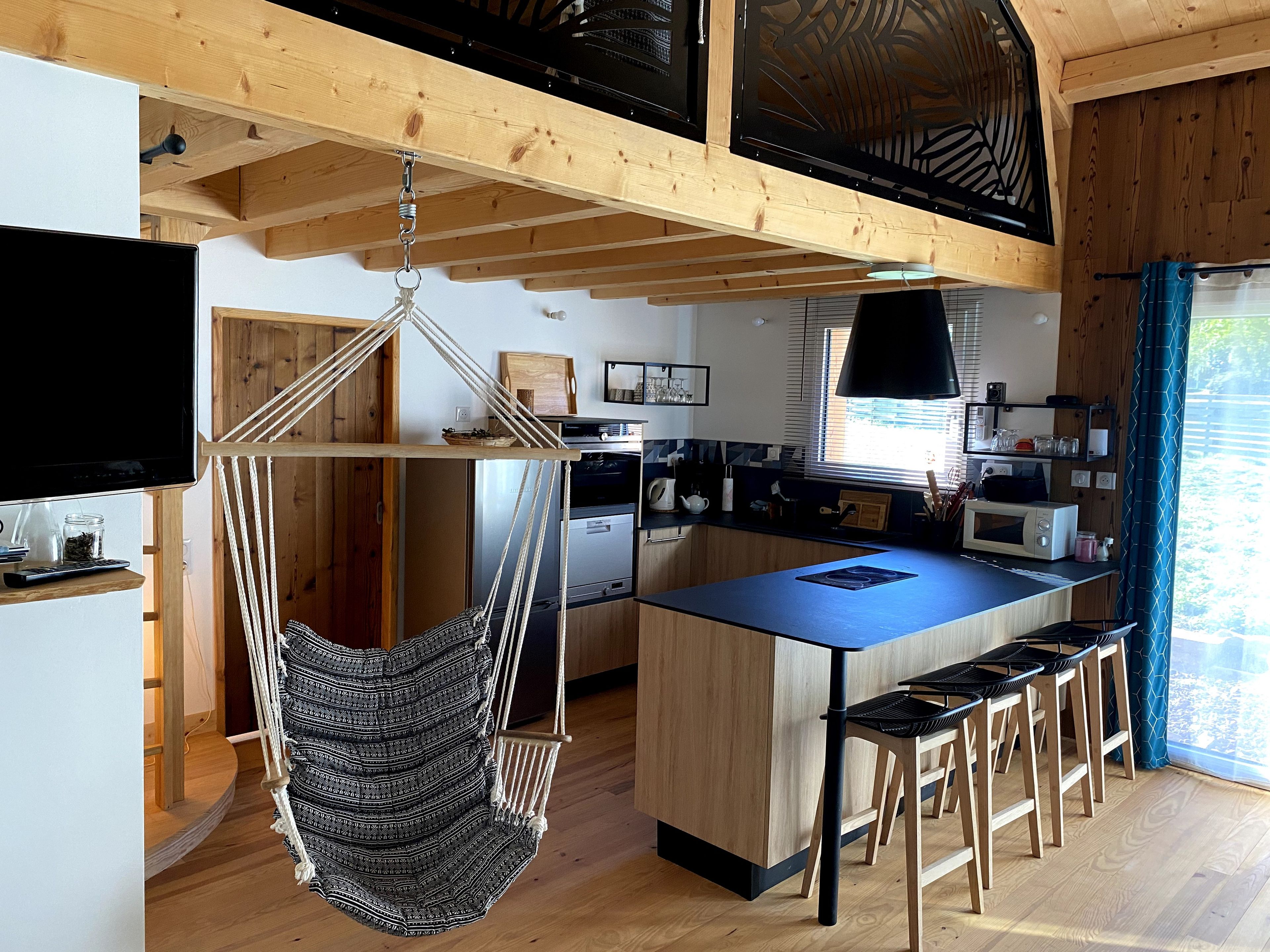 Une cuisine moderne dotée d’un îlot central, de planchers en bois et d’un fauteuil suspendu en macramé.