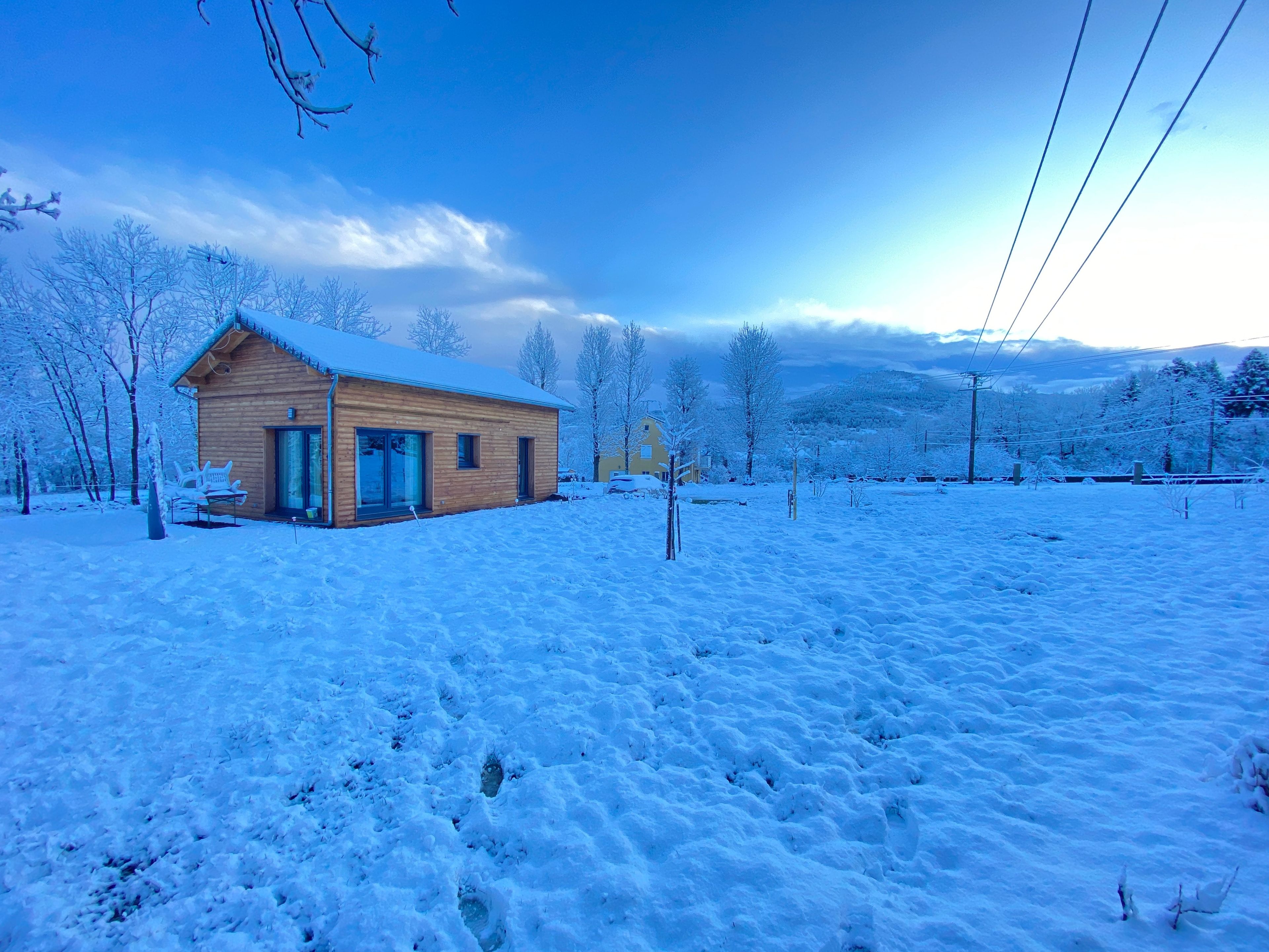 A wooden cabin with a snow-covered roof, surrounded by a snowy landscape and trees.