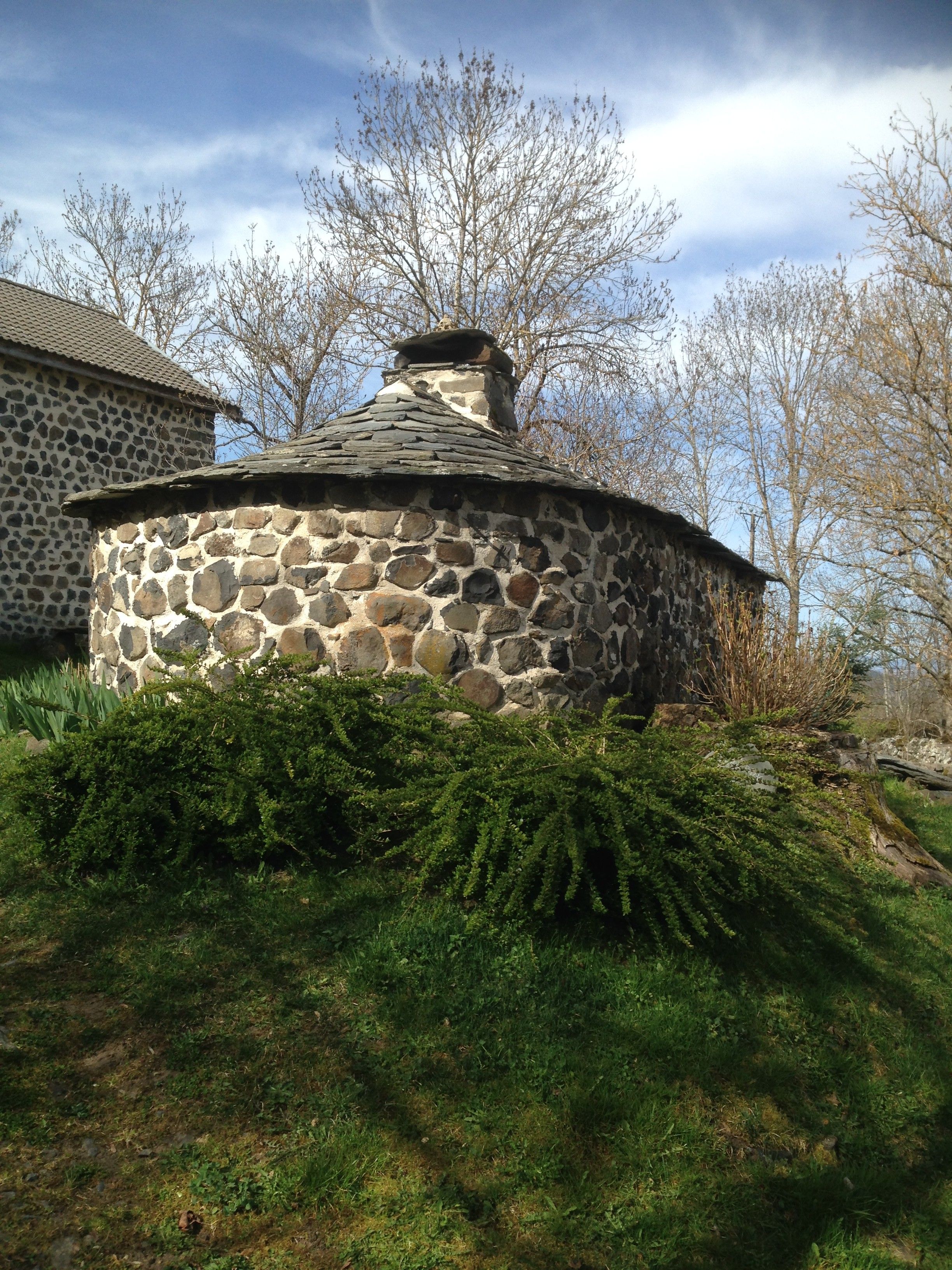 A stone structure with a conical roof, surrounded by greenery and trees.