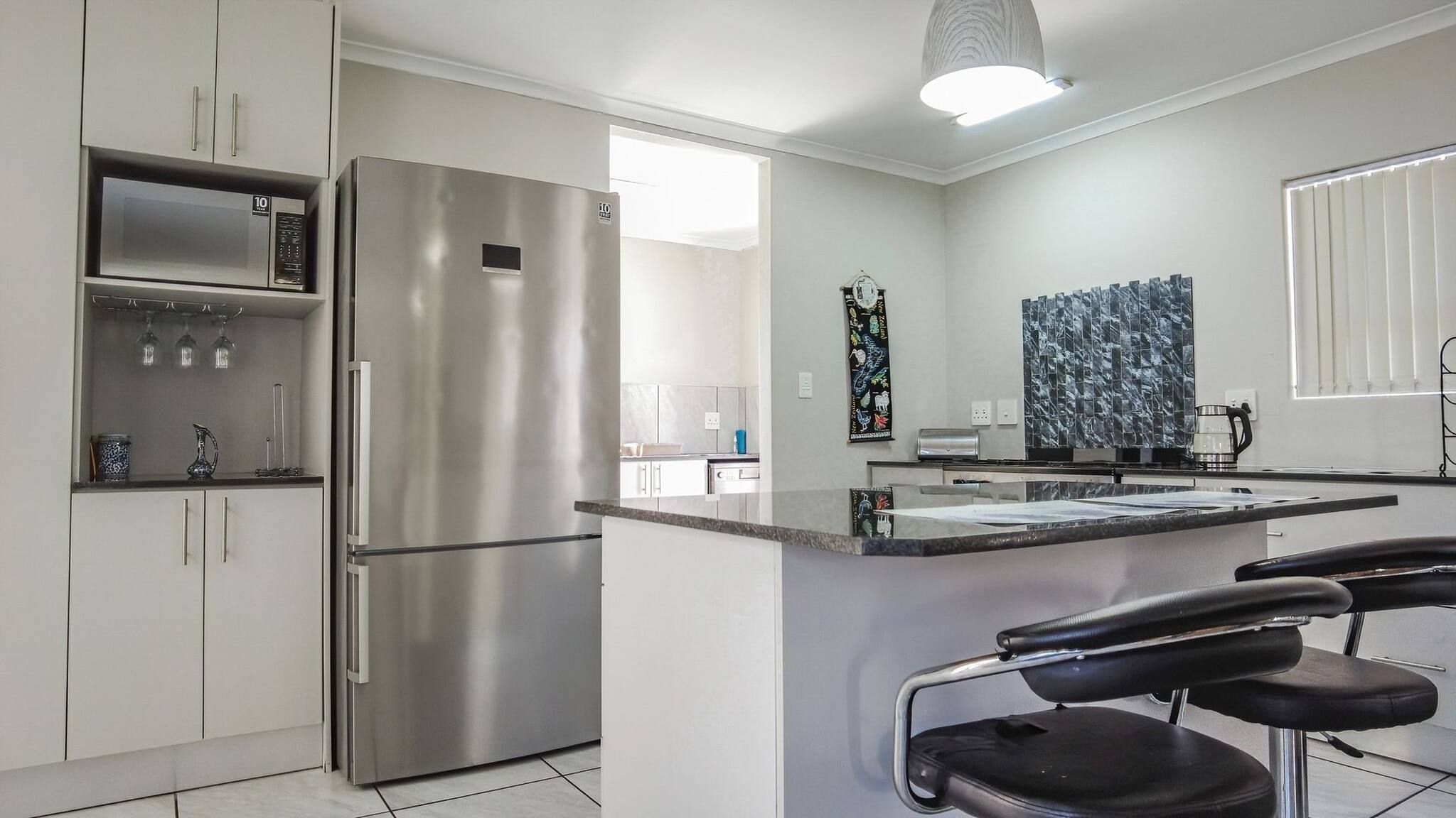 A modern kitchen with stainless steel appliances, a marble backsplash, and a bar area with stools.
