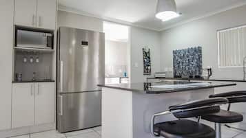 A modern kitchen with stainless steel appliances, a marble backsplash, and a bar area with stools.