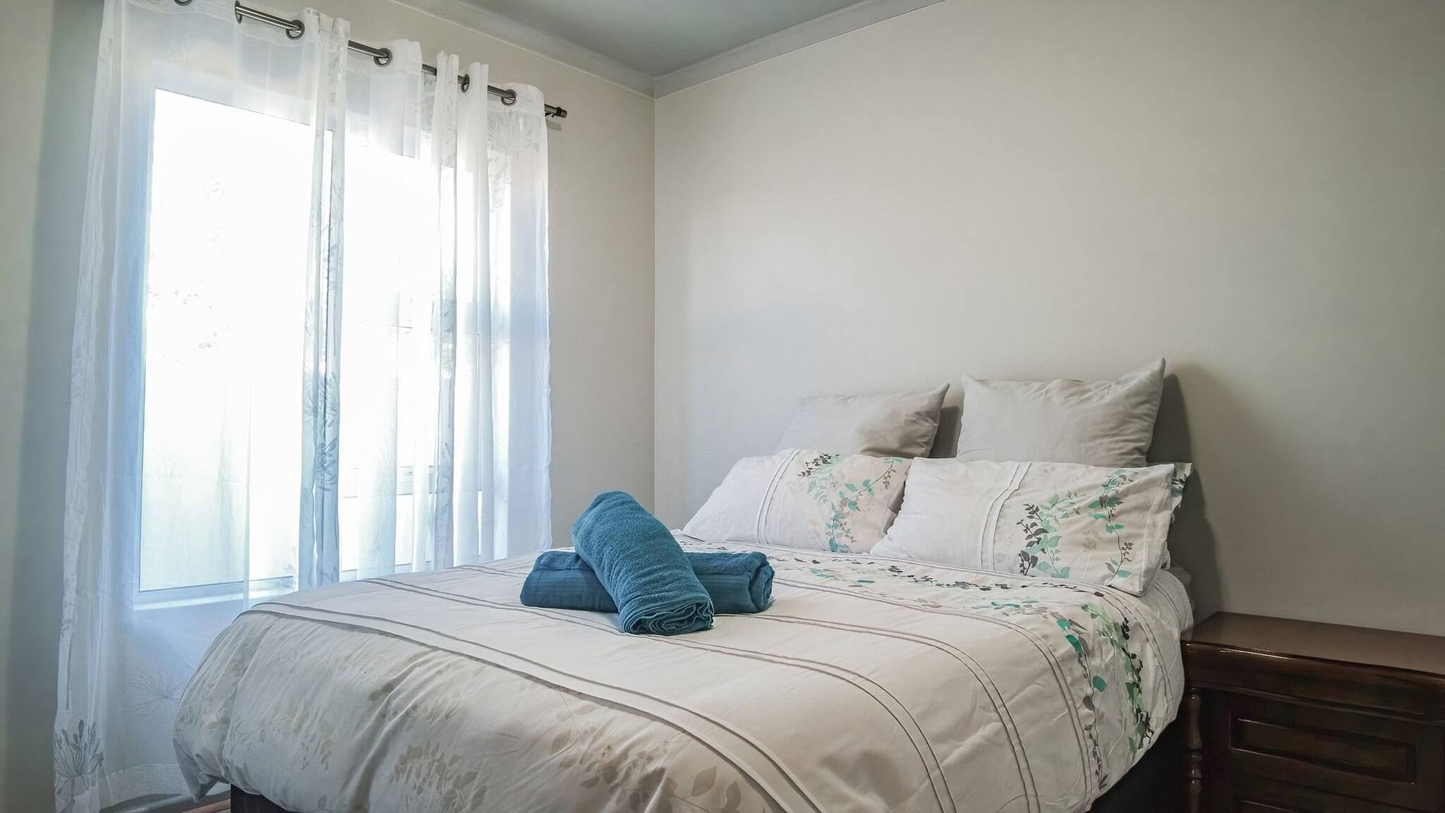 Une chambre à coucher avec un lit, une fenêtre avec des rideaux et une table de chevet.