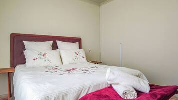 A neatly made bed with floral bedding and pillows, a wooden nightstand, and a red blanket.