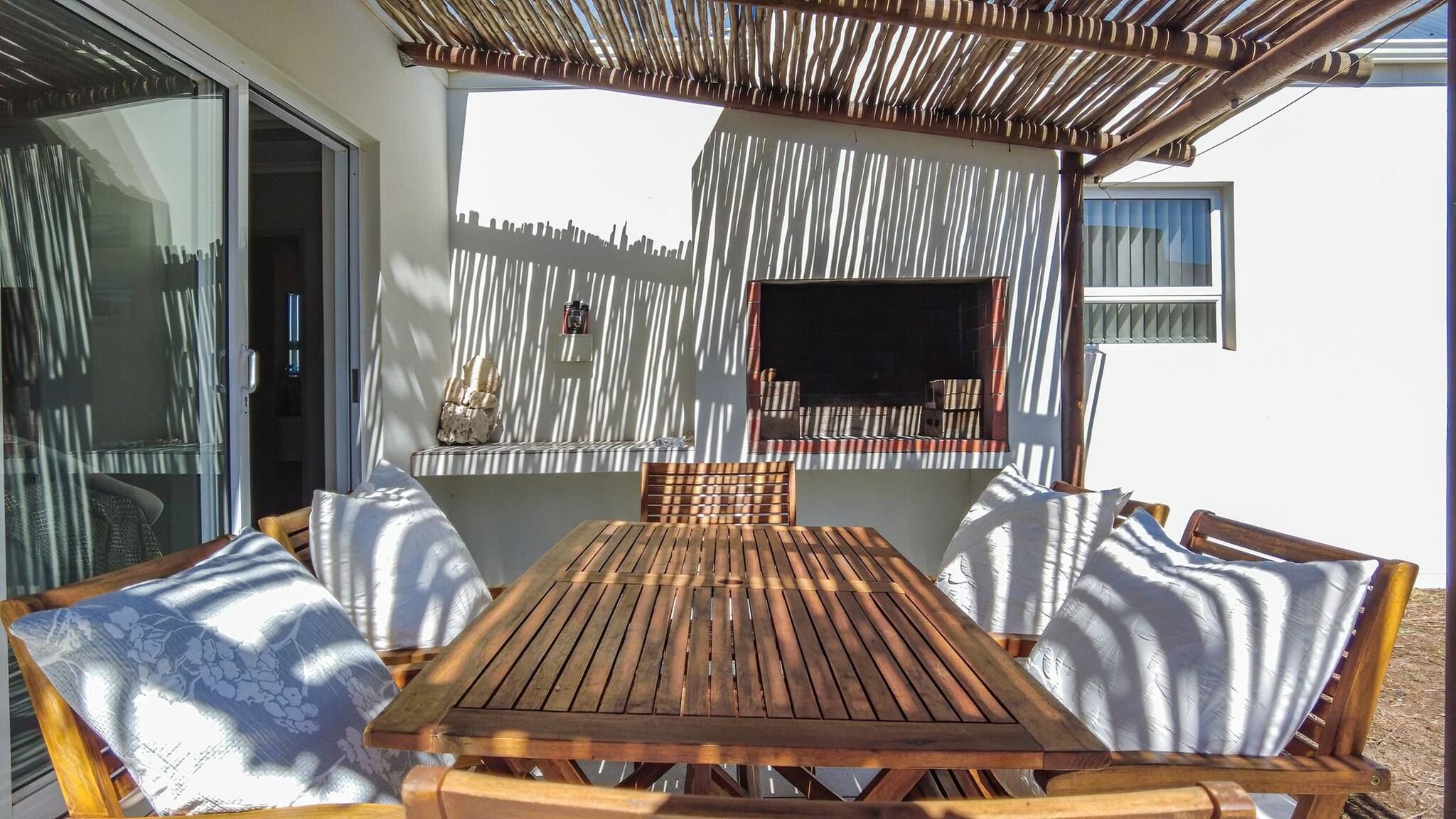 An outdoor patio with a wooden table and chairs, a TV mounted on the wall, and a decorative wall panel.