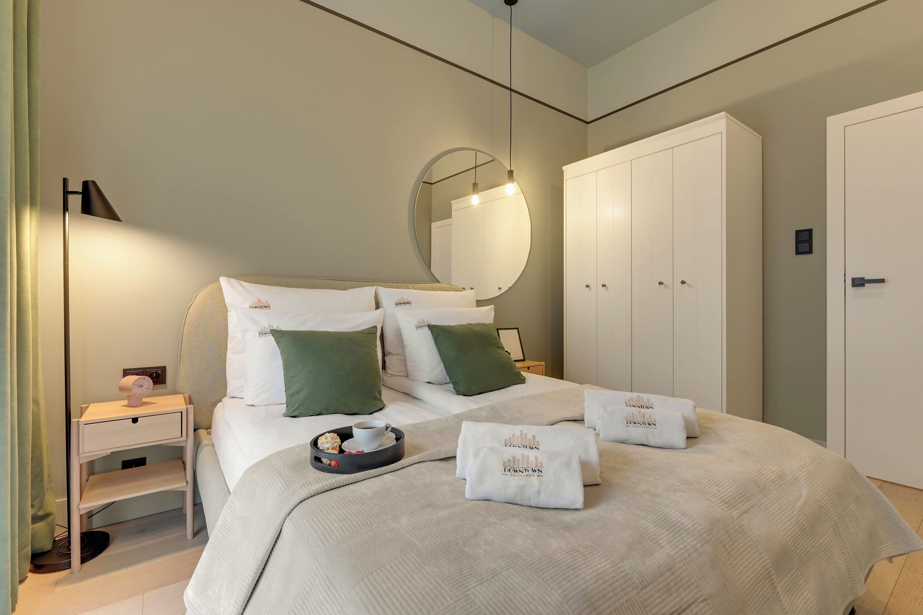 A hotel room with a bed, a bedside table, a lamp, a wardrobe, and a mirror.