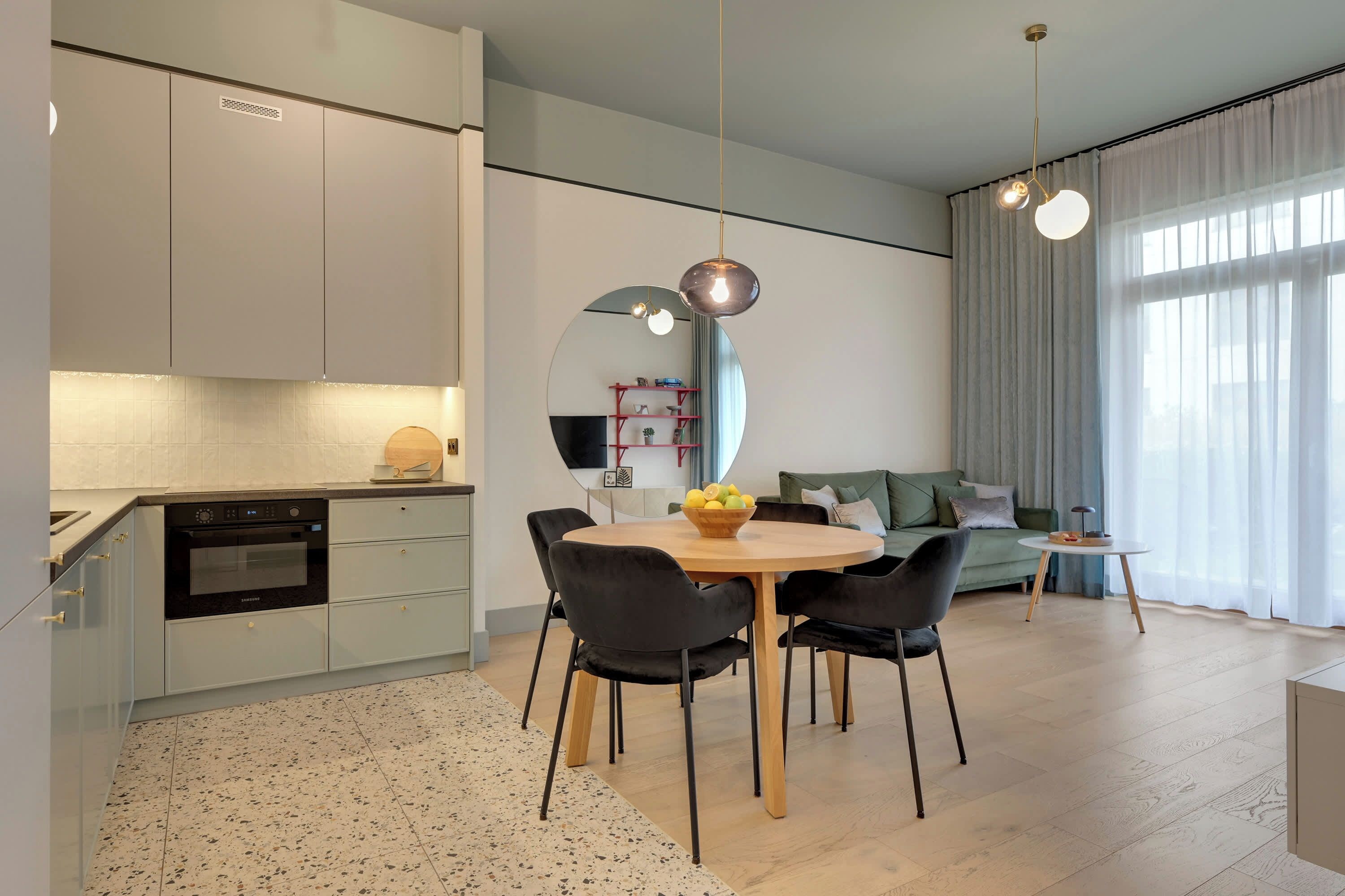 A modern kitchen with a dining area, a round table with chairs, and a large mirror.