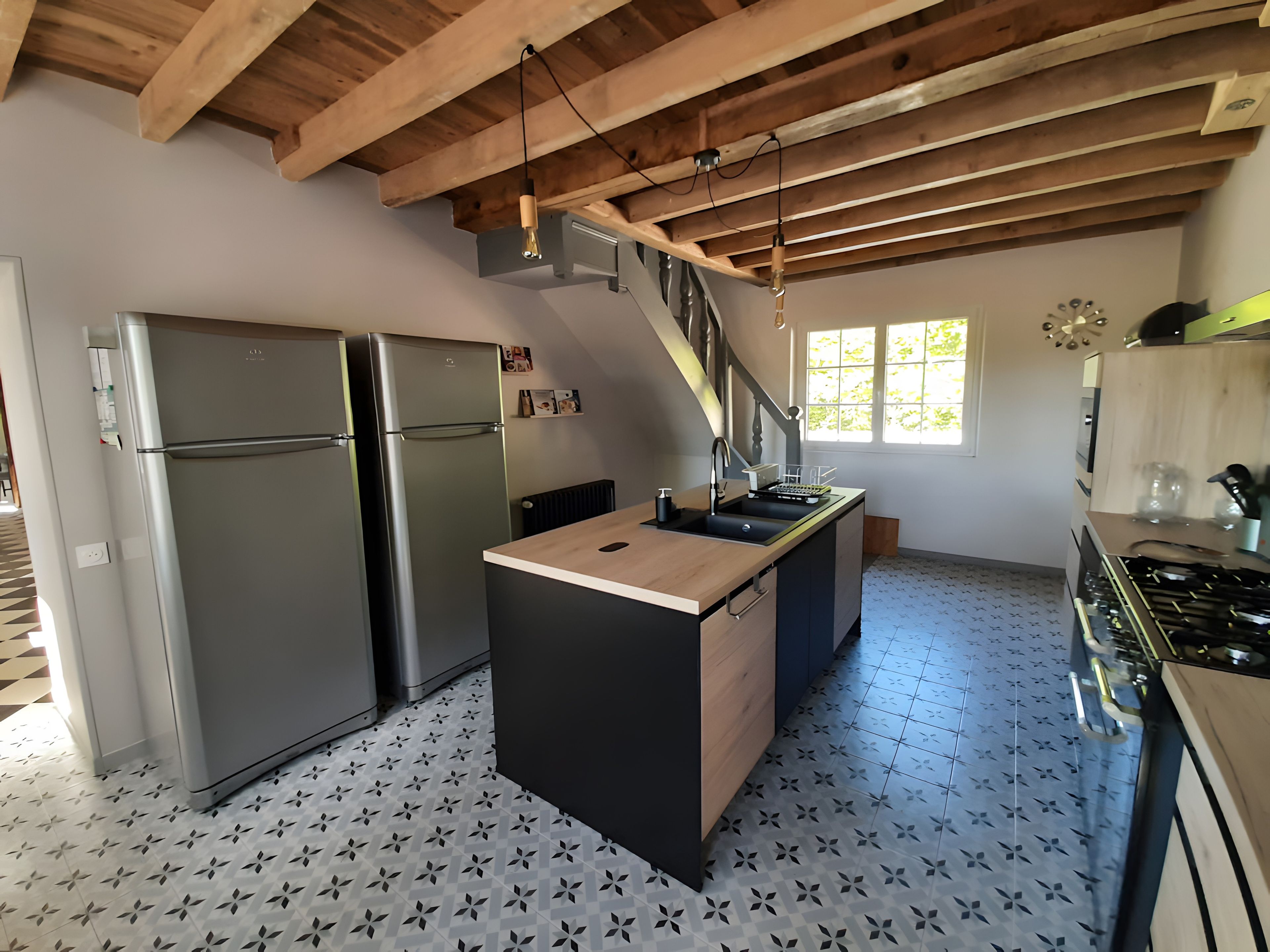 A kitchen with a central island, stainless steel appliances, a wooden ceiling, and patterned floor tiles.