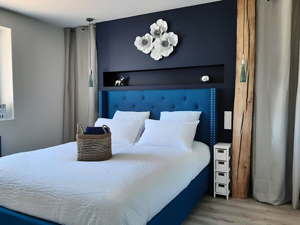 A modern bedroom with a blue headboard, white bedding, and a decorative wall piece.
