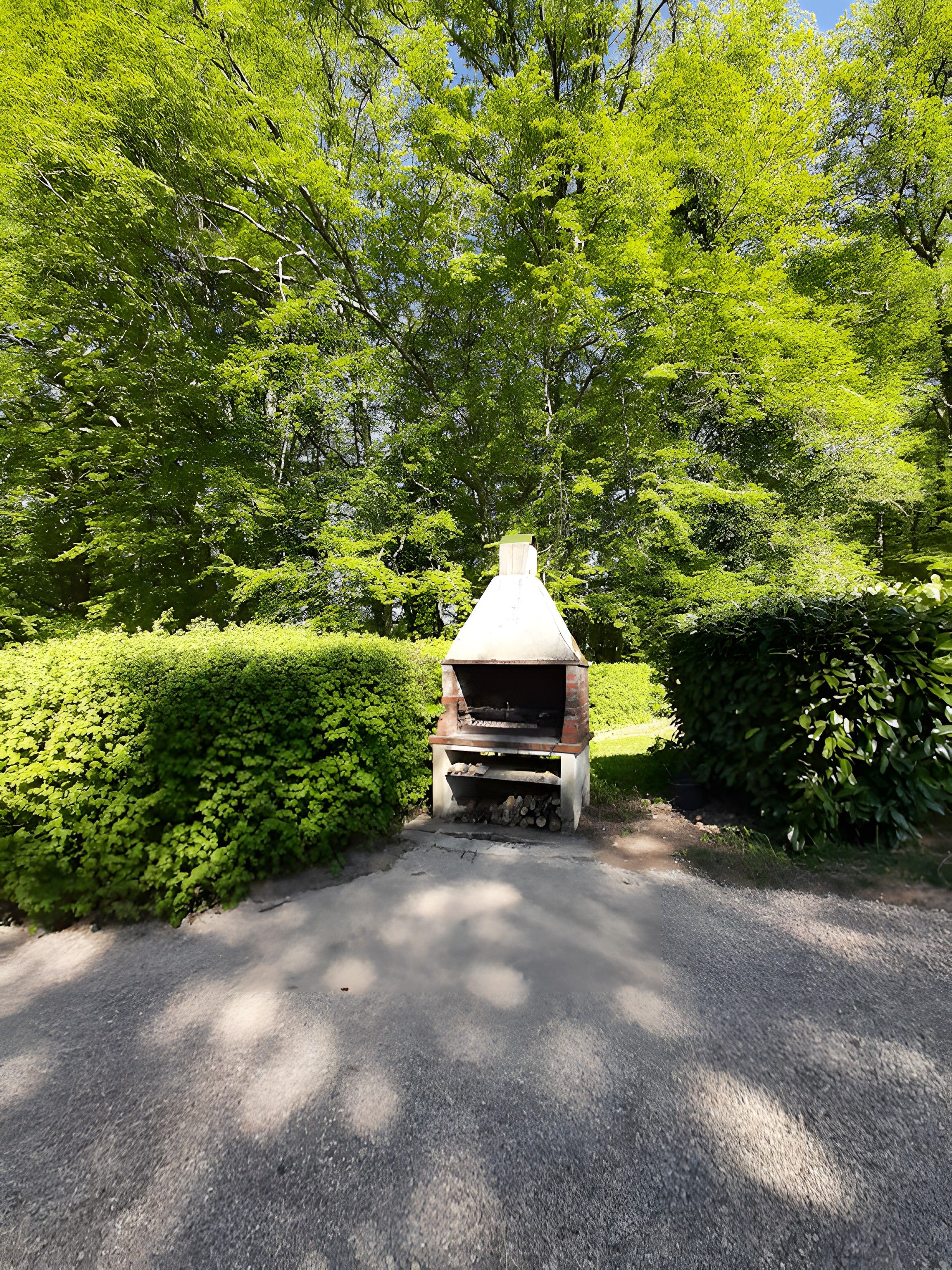 A brick barbecue grill in a landscaped area with a paved path.