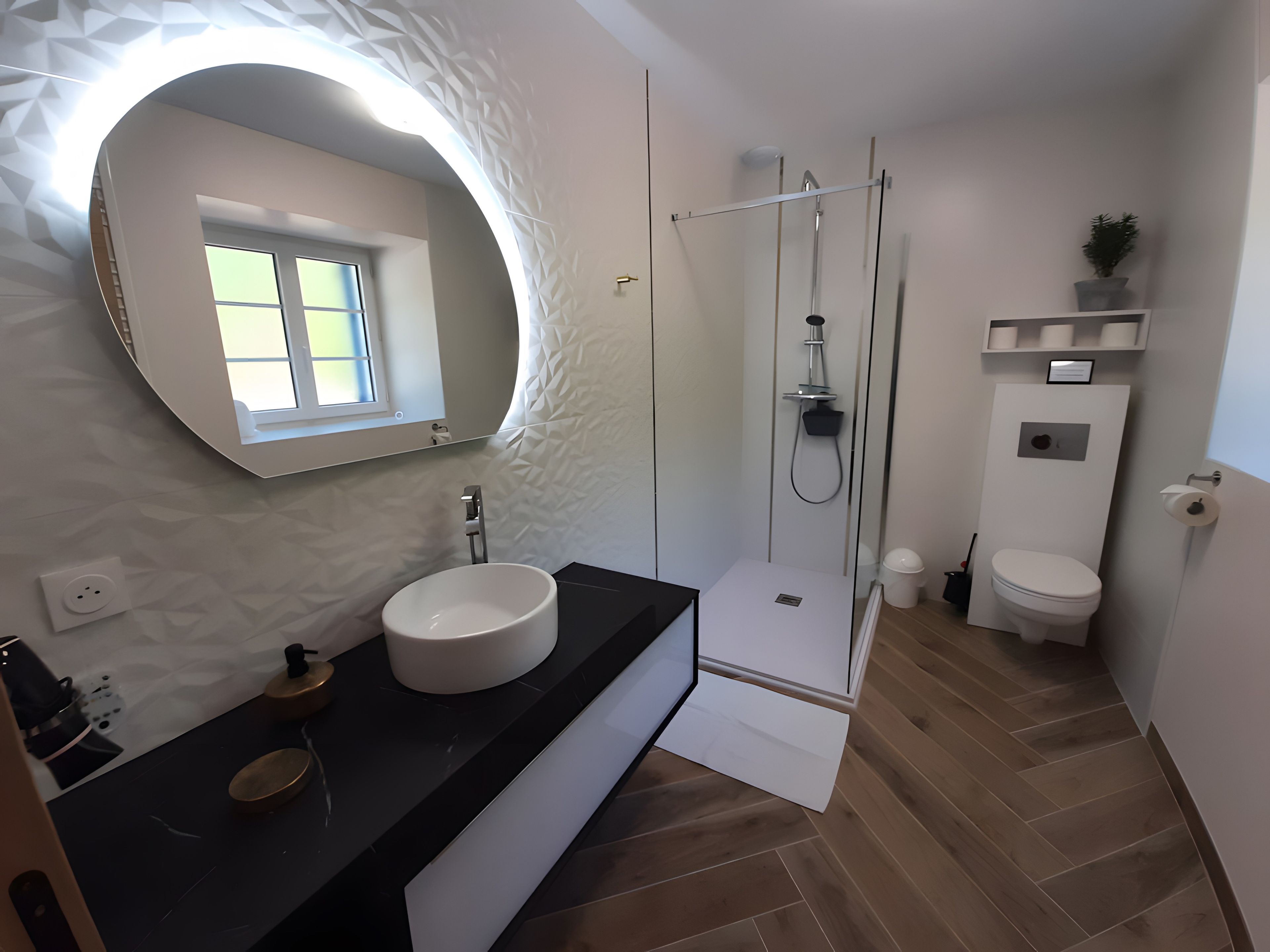 Une salle de bain moderne avec un grand miroir rond, un lavabo, une douche et des toilettes.