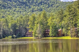 Una cabaña con varias edificaciones rodeada de bosque y un lago.