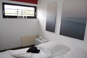 A bedroom with a bed, a nightstand, a window with a view, and a painting on the wall. - Holiday home with 2 bedrooms (Butjadingen)