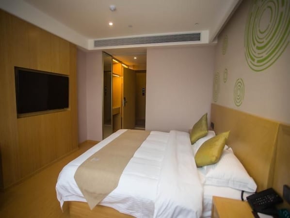 A hotel room with a large bed, a flat-screen TV, a bedside table, and a door leading to a bathroom.