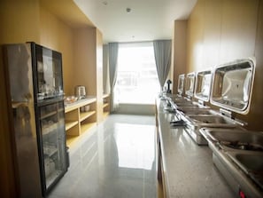 A modern kitchen with a refrigerator, a buffet counter, and a window with curtains.