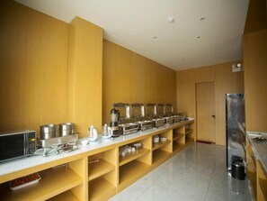 A hotel kitchen with a buffet setup, including a microwave, various food containers, and a refrigerator.