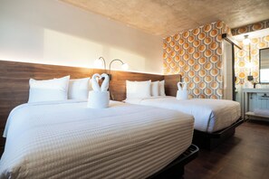 Hotellihuone, jossa on kaksi sänkyä, puinen pääty, kuvioitu seinä ja pieni kylpyhuone.