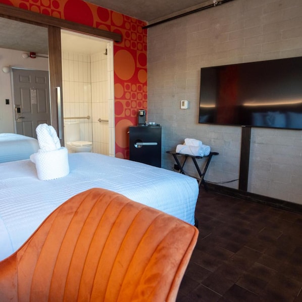 Habitación de hotel con cama, una silla, baño con inodoro y televisor montado en la pared.