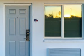 Una puerta con un ojo de cerradura y un mirilla, una ventana con vista al atardecer, y un letrero pequeño con el número 110.