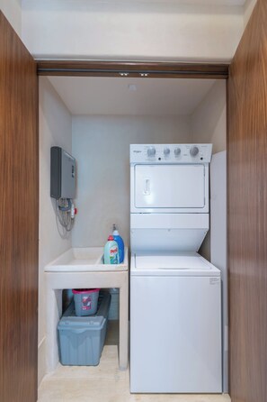 A compact laundry room with a washer and dryer, a utility sink, and a water heater. - Artila Isla Mujeres: Luxury Beachfront Residence in Isla Mujeres (Isla Mujeres)