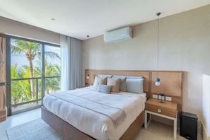 A modern hotel room with a large bed, a nightstand, a lamp, and a view of palm trees through the window. - Artila Isla Mujeres: Luxury Beachfront Residence in Isla Mujeres (Isla Mujeres)