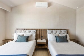 A hotel room with two beds, wooden headboards, a nightstand with a lamp, and a ceiling air conditioning unit. - Artila: Oceanfront Penthouse with Rooftop (Cancún)