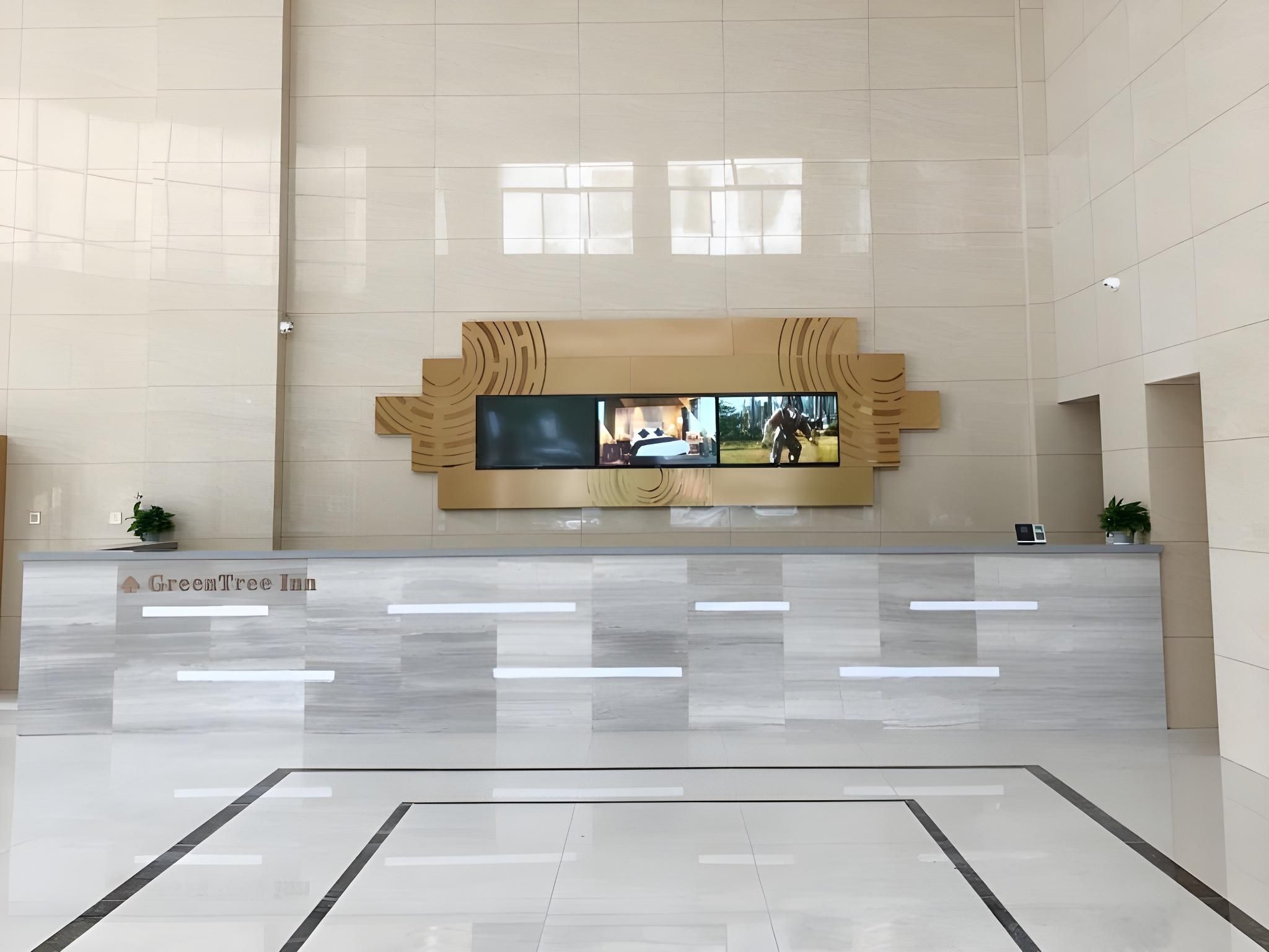A hotel reception area with a modern design, a large flat-screen TV mounted on the wall, and a reception desk.