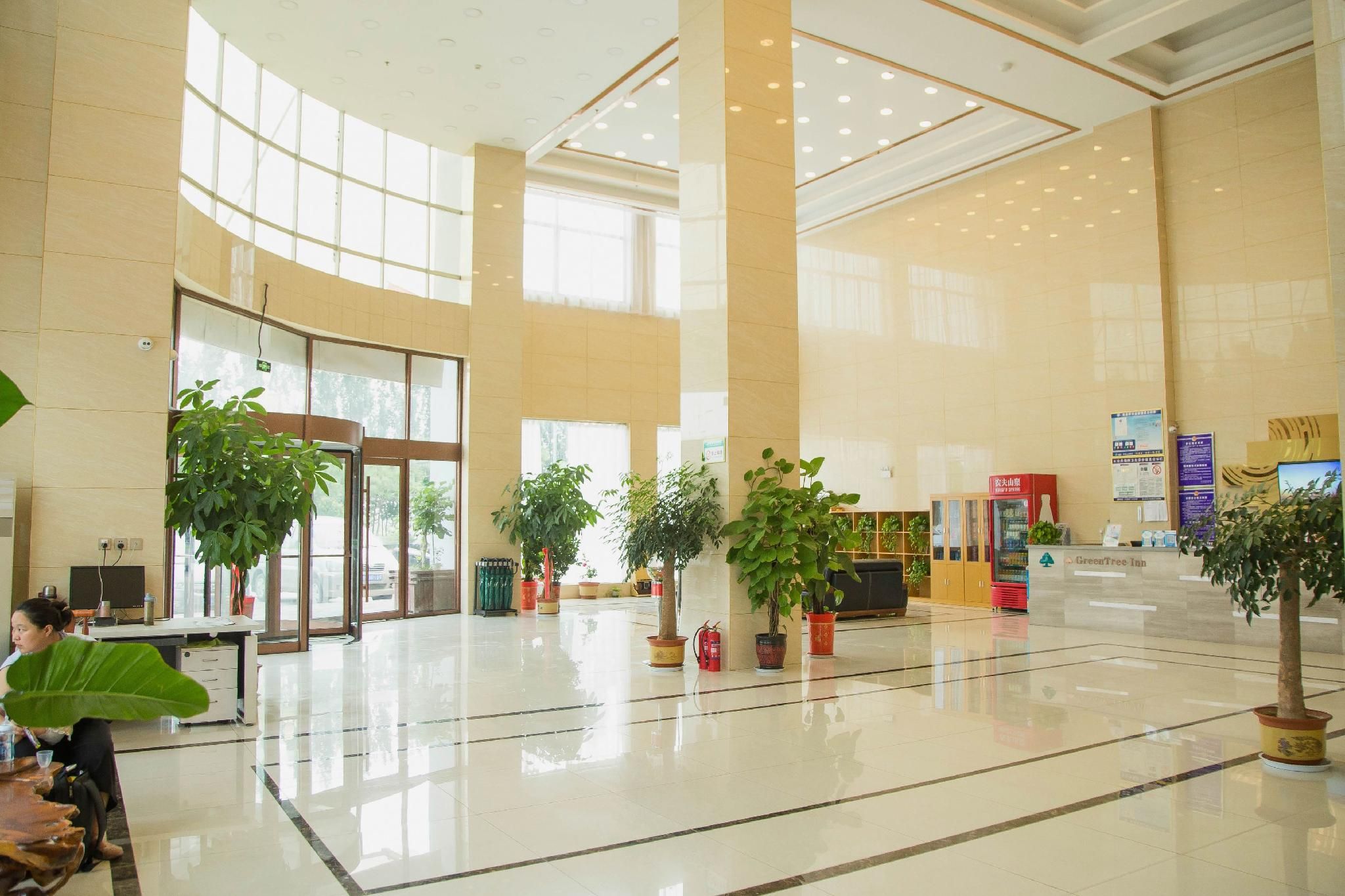 A spacious lobby with high ceilings, large windows, and multiple potted plants.