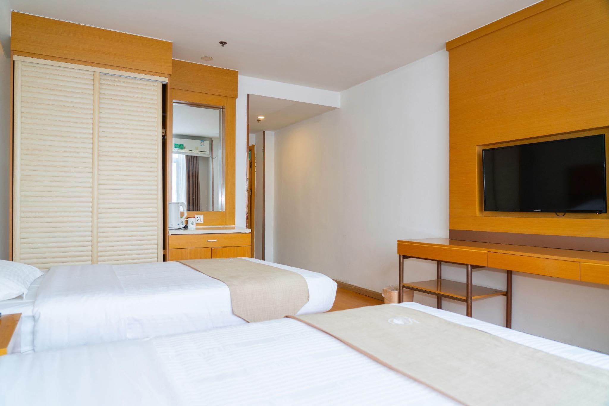 A hotel room with two beds, a TV, a desk, and a bathroom visible through an open door.