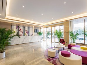 A modern hotel lobby with a marble reception desk, seating area with colorful cushions, and large windows offering a view of the city. - Lavande Hotel (Guangzhou)
