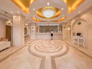 Un vestíbulo de hotel con mostrador de recepción, una araña de cristal y un diseño de piso circular.