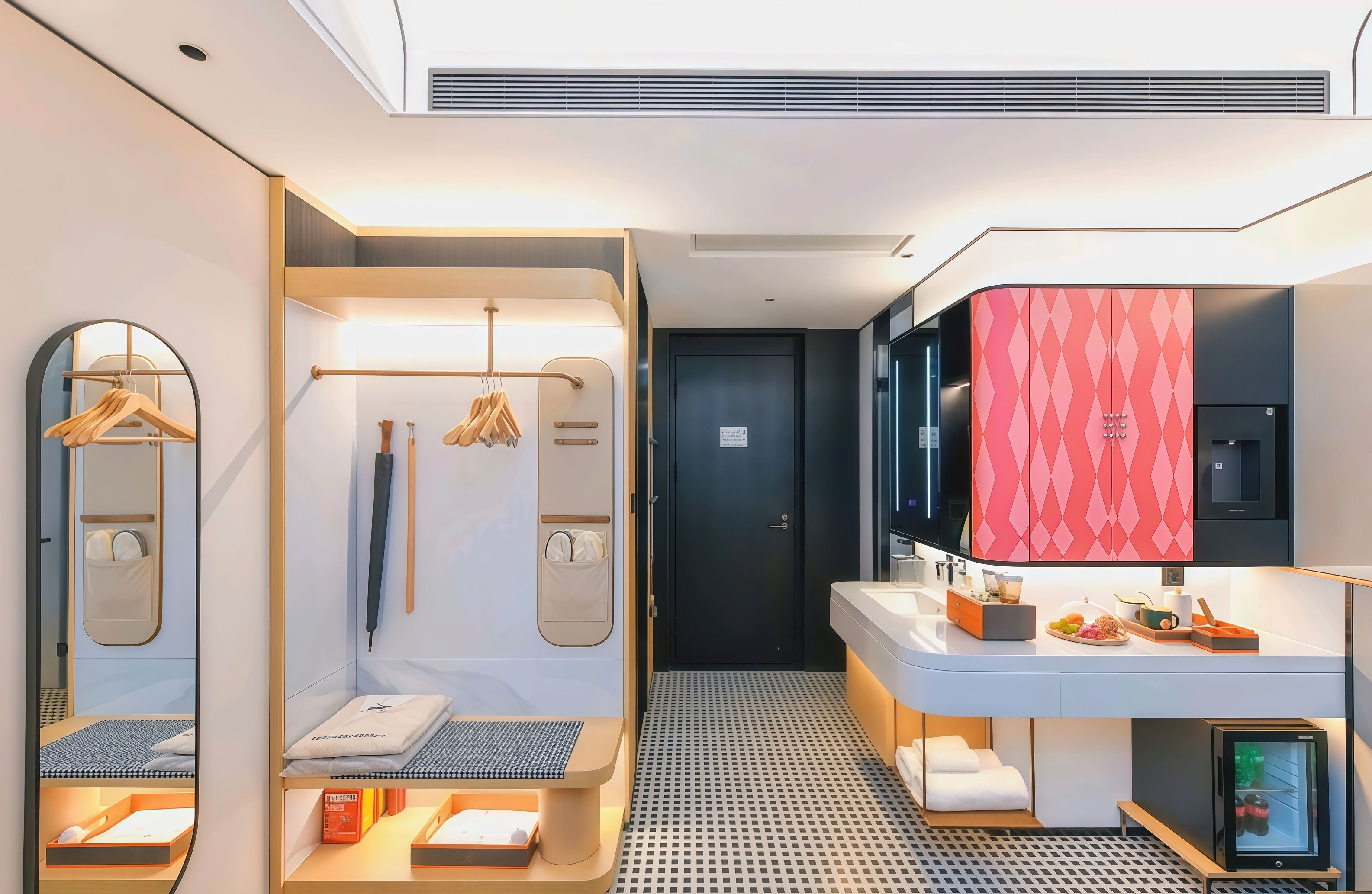 A modern hotel room with a walk-in closet, a large mirror, a vanity with a sink, and a small refrigerator.