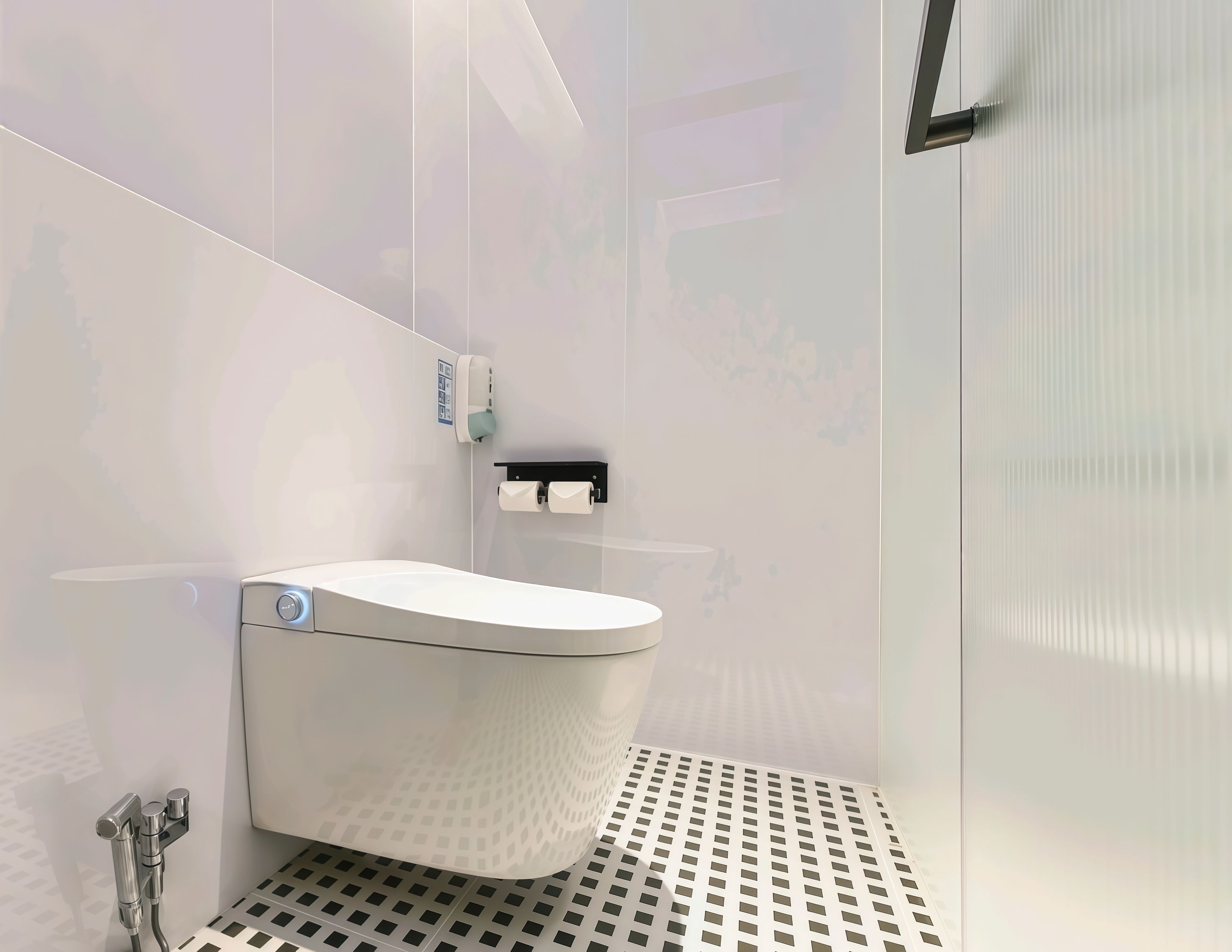A modern bathroom with a white toilet, a hand dryer, and a paper towel dispenser.