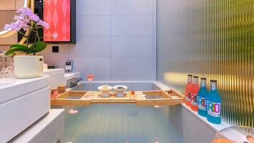 A modern bathroom with a bathtub, a potted orchid, a wine glass, and a tray with snacks.
