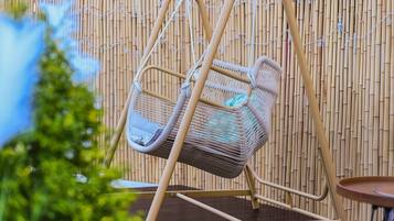 A wicker swing chair with a cushion, set against a bamboo fence backdrop.