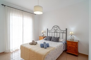 A neatly made bed with a headboard, two bedside tables with lamps, and a window with sheer curtains. - Apartment in Nerja by Burriana Beach (Nerja)
