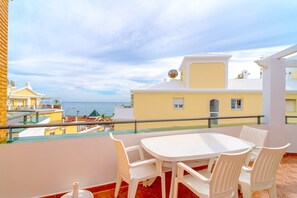 A balcony with a white table and chairs, overlooking a coastal area with buildings and the sea. - Apartment in Nerja by Burriana Beach (Nerja)