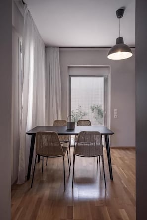 Un comedor con una mesa y cuatro sillas de mimbre, una ventana con cortinas, y una lámpara colgante.