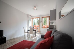 A modern living room with a grey sofa, red cushions, a red rug, a television, and a dining area with a table and chairs. - Appartamento Venier (Venice)