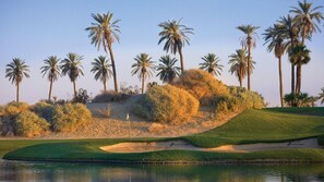 Un campo de golf con búnkeres de arena, un cuerpo de agua y palmeras.