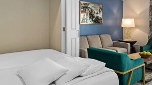 Habitación de hotel con cama, dos sillones, una mesita de noche con lámpara y un cuadro en la pared.