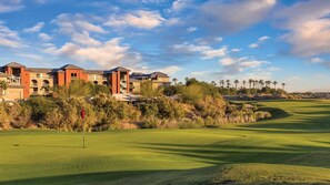 Un parcours de golf doté d’un club-house comprenant plusieurs bâtiments, entouré de palmiers et offrant une vue sur un ciel dégagé.