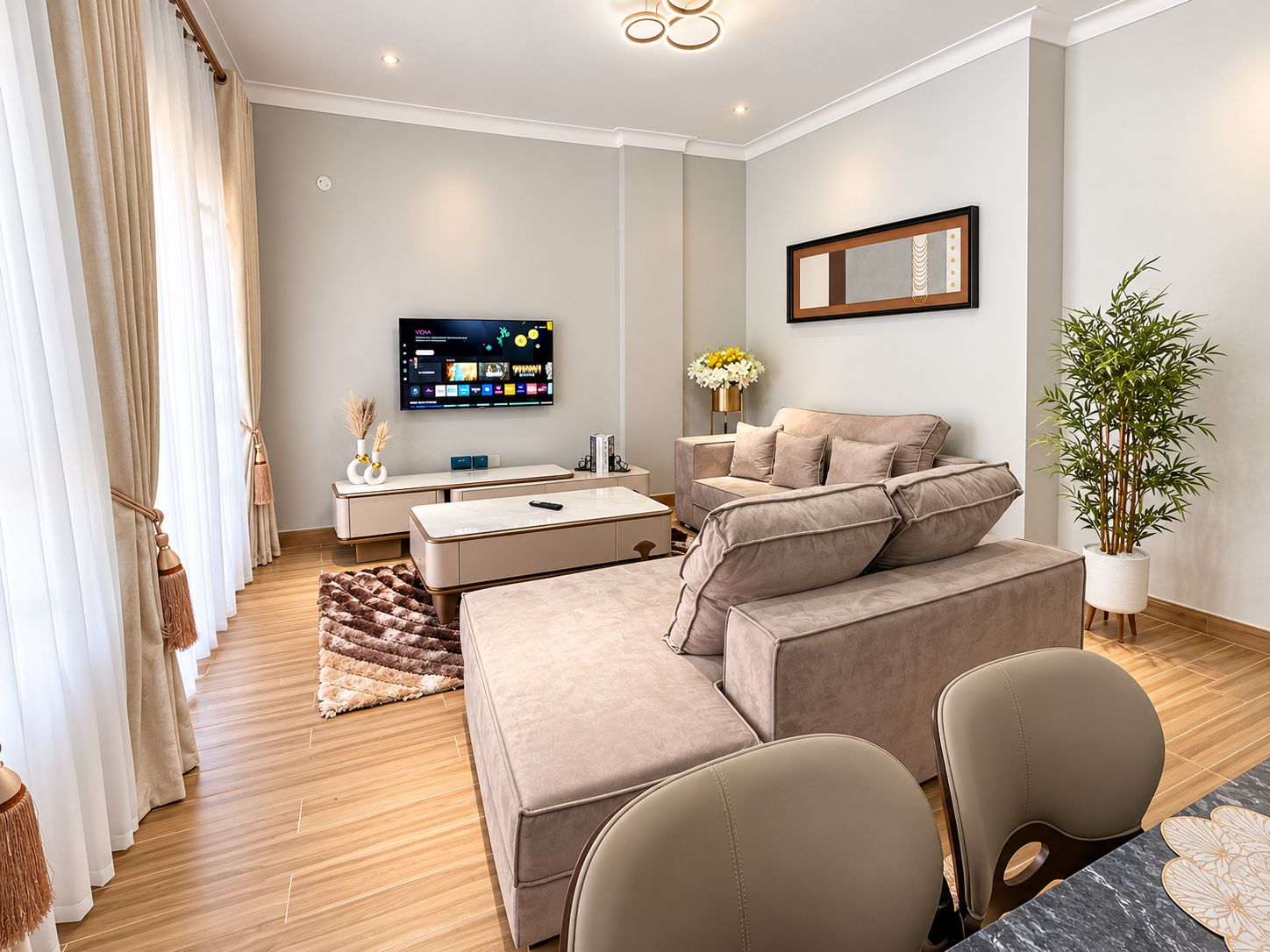 A modern living room with a sofa, armchairs, a TV, and a potted plant.