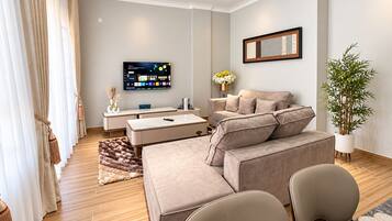 A modern living room with a sofa, armchairs, a TV, and a potted plant.