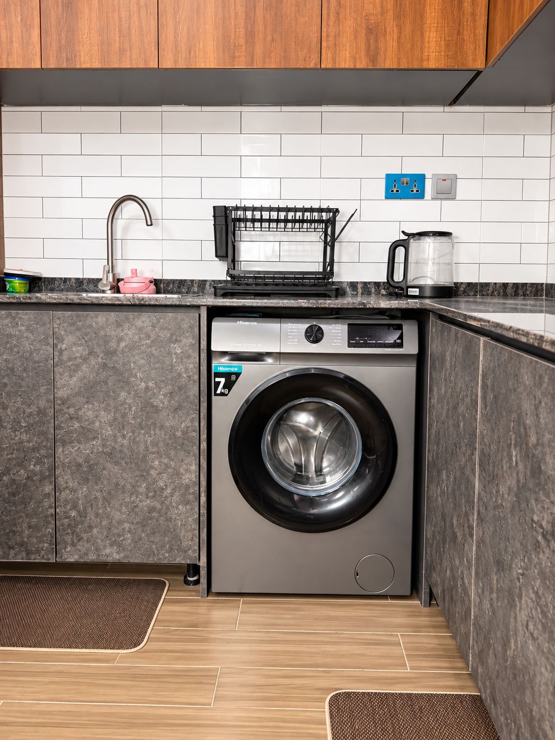 A compact kitchen with a built-in washer and dryer, a stainless steel sink, and a black coffee maker on the countertop.