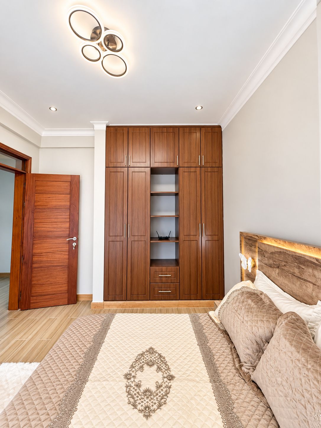 A bedroom with a large wardrobe, a bed with a headboard, and a decorative wall light.