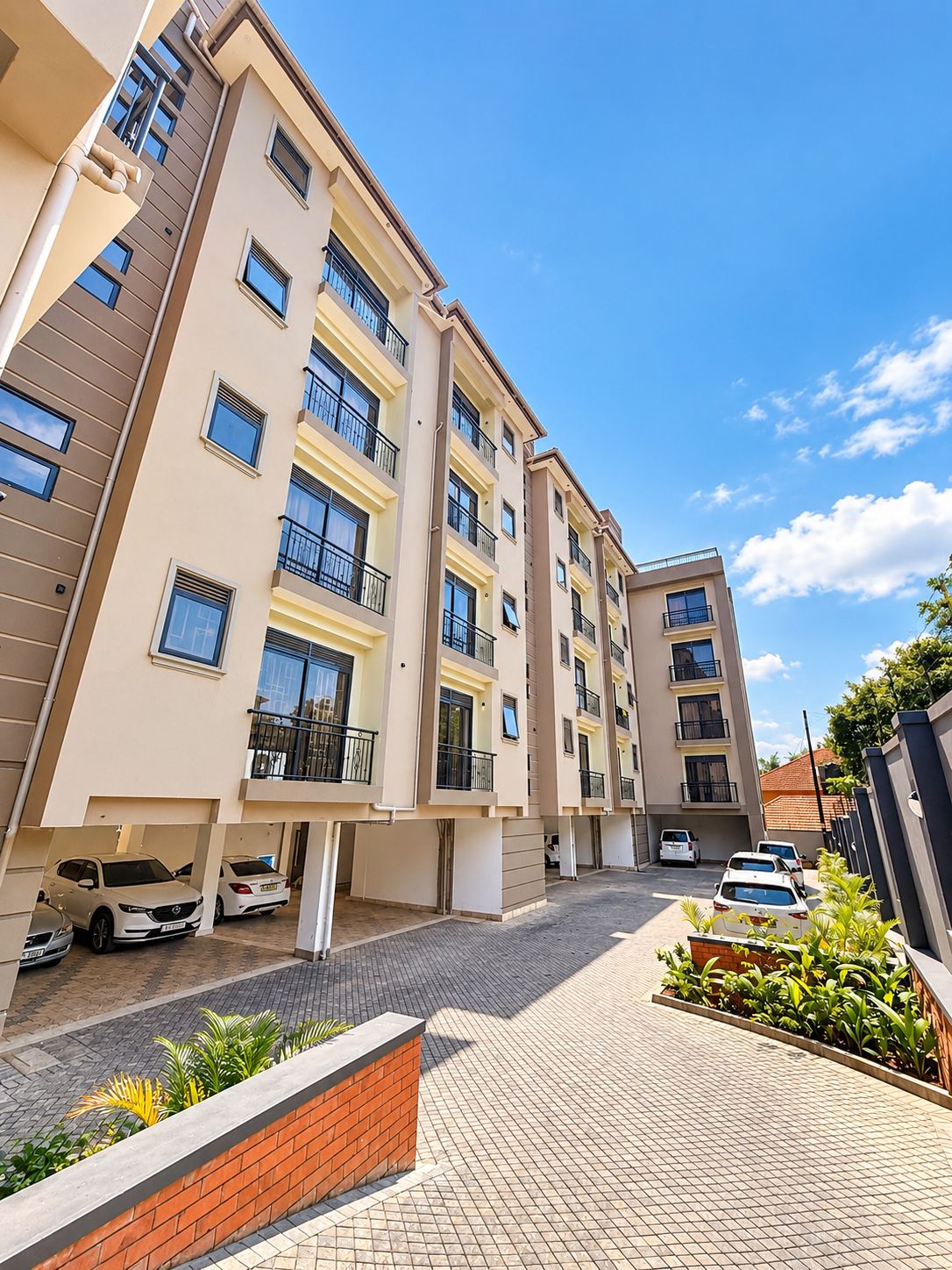 A multi-story residential building with balconies, a paved driveway, and parked cars.